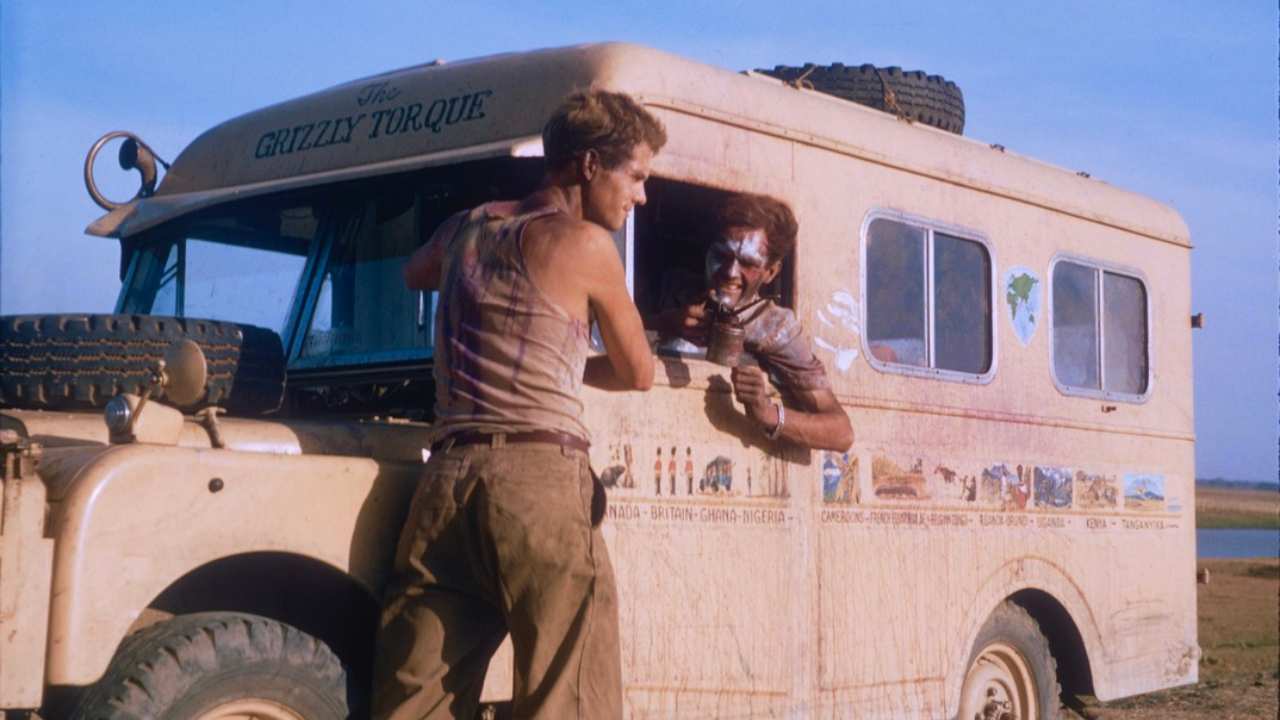 a man leaning on a bus talking to another man